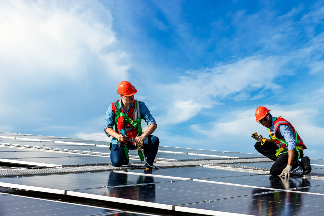deux techniciens aux casques rouges qui installent un panneau solaire sur un toit