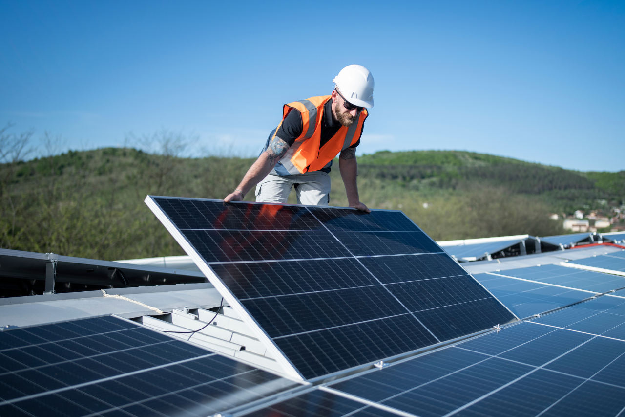 technicien qui porte et pose un panneau solaire sur un toit