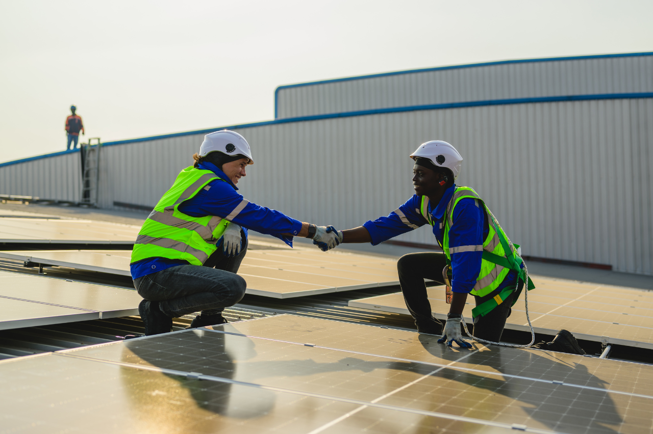 deux personnes qui se serrent la main sur un toit où sont posés des panneaux solaires